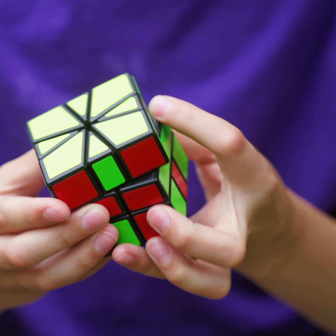 Boy in blue t-shirt holding Rubik's cube. Teenage boy playing with square colorful toy. Rubik's cube in new form in child's hands. Close-up.