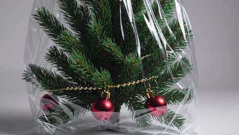small decorated christmas tree wrapped in transparent plastic film, symbolizing consumerism, environmental issues, and artificiality of modern holidays