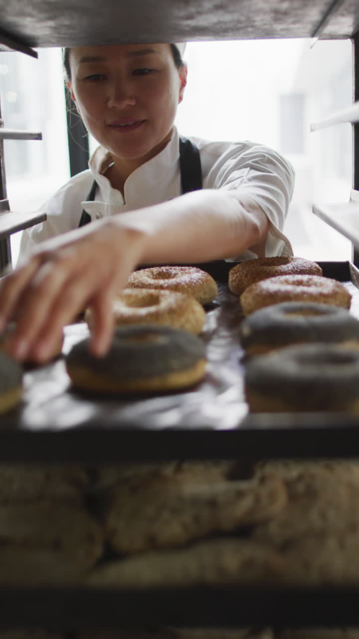 Vídeo vertical de padeira asiática feliz preparando donuts na padaria