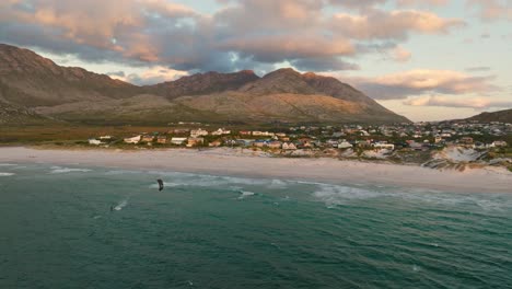 a kitesurfer riding during sunset in front of pringles bay town, drone shot