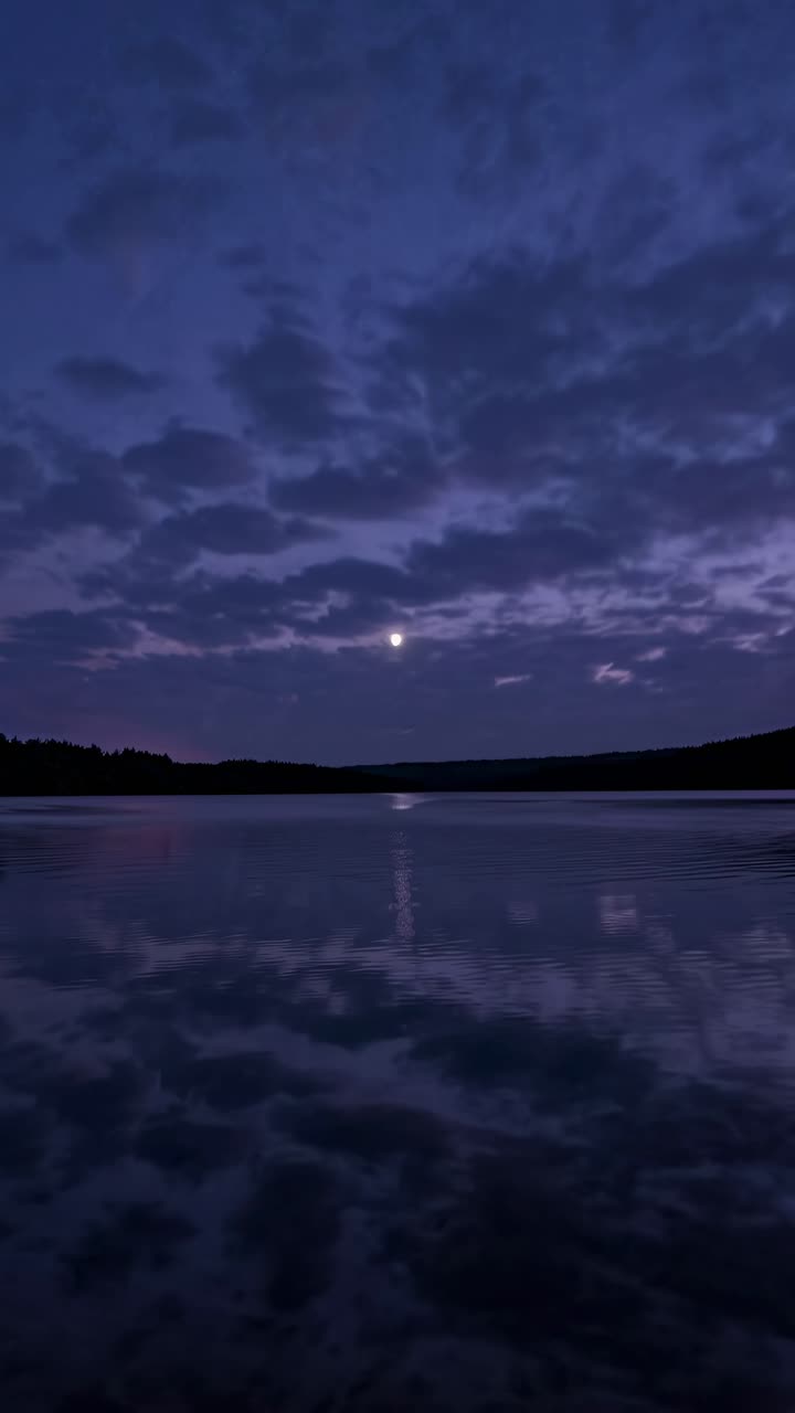 Um pôr do sol sereno sobre um lago com um céu roxo e laranja, capturado de um ângulo baixo.