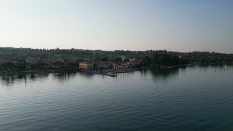 Flying-Over-Lago-di-Garda-With-Coastal-Town-And-Hotels-In-Cisano,-Province-of-Verona,-Italy