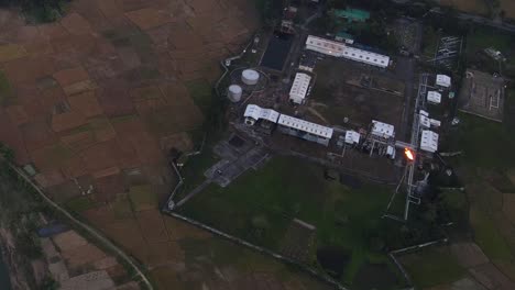 Aerial-view-of-gas-plant-in-the-middle-of-rice-paddy-field-on-the-bank-of-Surma-river-after-sunset,-Bangladesh