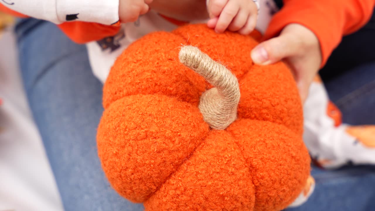 Close up of baby hands touching a fabric pumpkin held by female hands as a sensory moment discovering textures