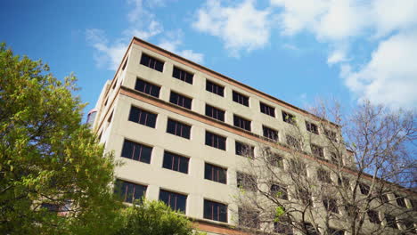 An-upward-perspective-of-a-tan-office-building-with-trees-and-sky