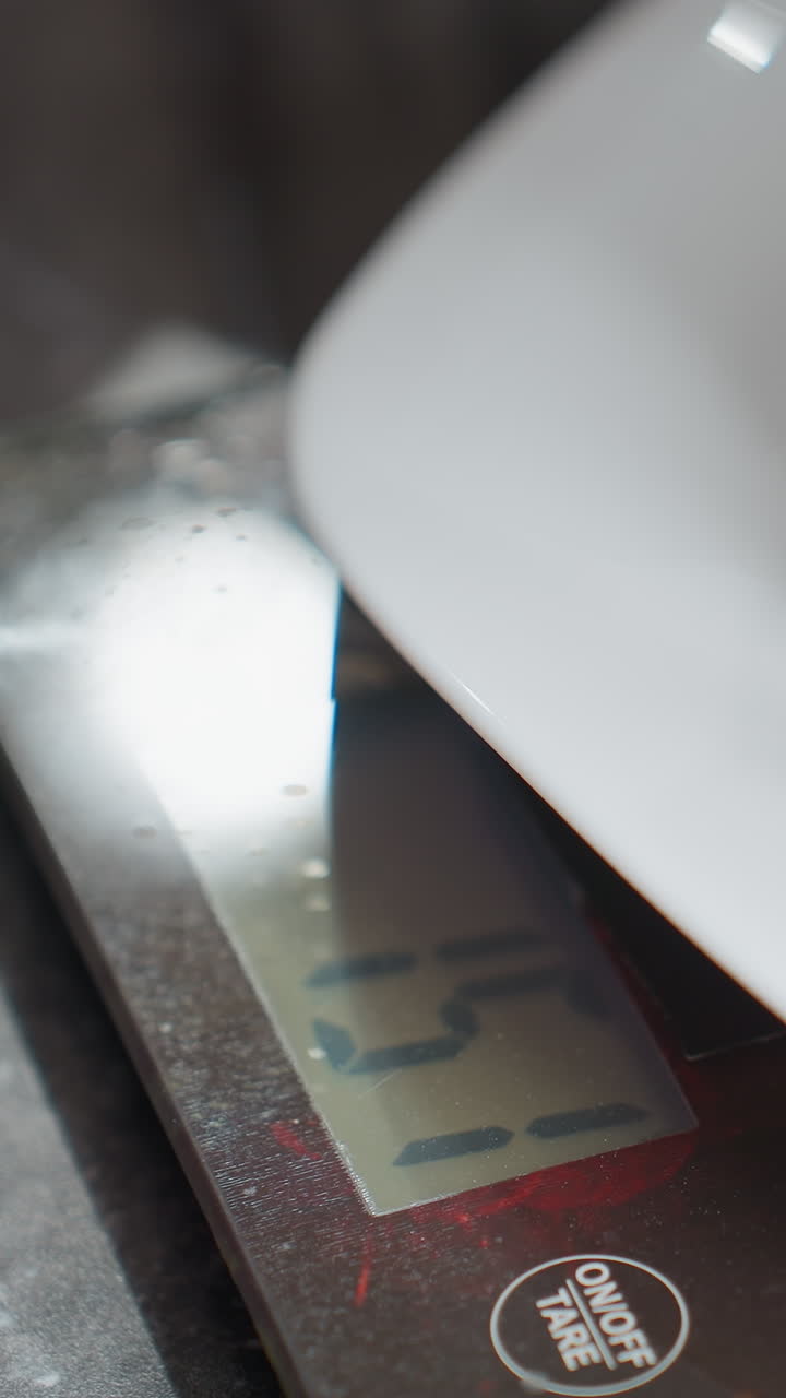 primer plano de un tamiz de acero inoxidable colocado en una placa blanca encima de una balanza de cocina digital que muestra el peso, configuración de la cocina con encimera moderna, balanza electrónica con botón de tare visible