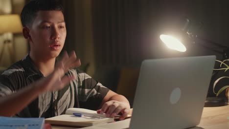 teenage boy learning online from laptop, raising hand distance learning online at virtual lesson class with teacher tutor on laptop by video conference