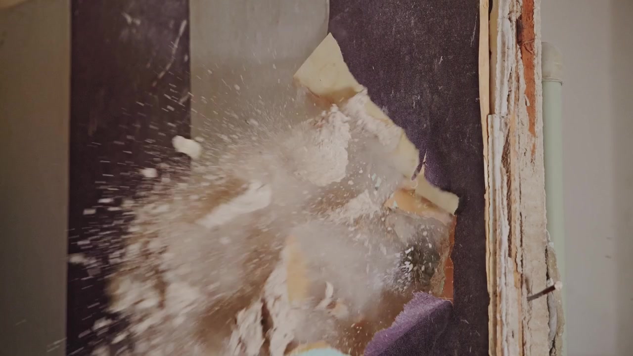 La slow motion cattura l'impatto drammatico mentre polvere e detriti esplodono dal muro.