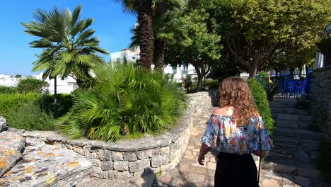 Walking-in-the-street-of-the-heritage-site-of-Alberobello,-following-a-young-blond-woman