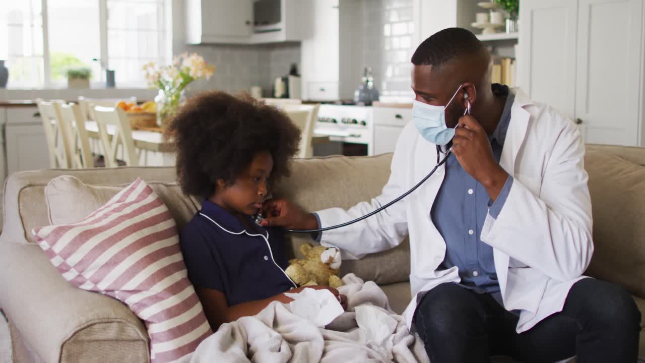 African american doctor wearing face mask using stethoscope to treat a sick girl at home