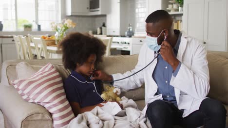 african american doctor wearing face mask using stethoscope to treat a sick girl at home