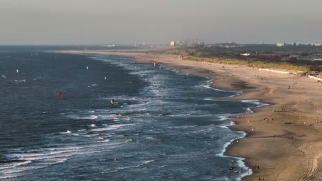 Kite-surfers-fly-and-ride-rough-windy-waves-in-murky-blue-ocean-in-sunset