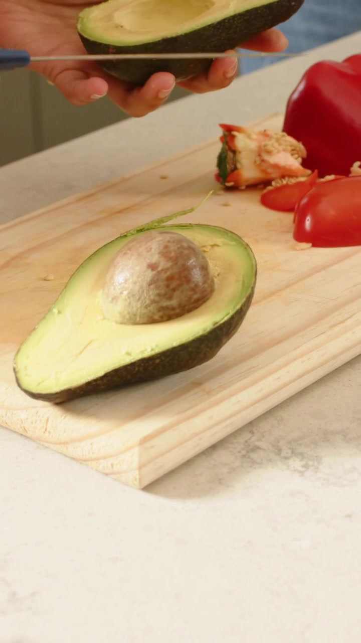 Video verticale: Mani con top di jeans che ruotano e allineano un avocado in cucina, un coltello entra per rimuovere il nocciolo