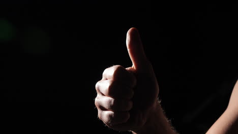 Close-up-of-hand-thumbs-up-illuminated-on-black-background