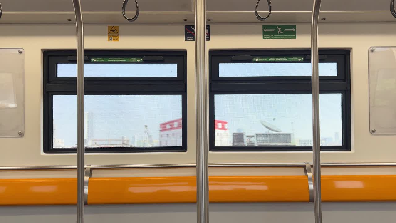 Static interior subway shot with empty orange seats and passing Bangkok cityscape through window