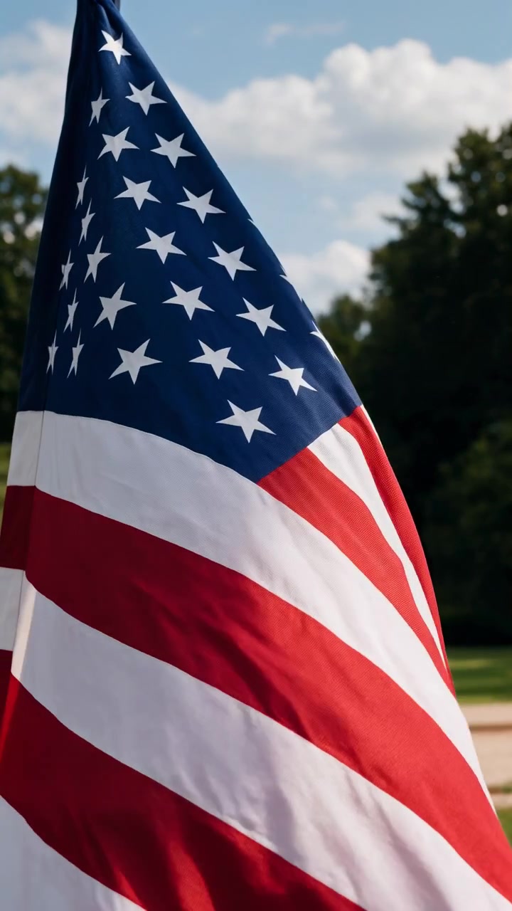 Una bandiera americana che sventola dolcemente al vento, sullo sfondo di un sereno e patriottico scenario esterno con alberi e un cielo limpido. Questa scena pacifica è per le festività nazionali e per ricordare