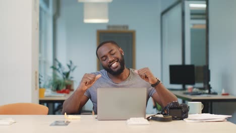 happy photographer working on computer at coworking. black man looking photos.
