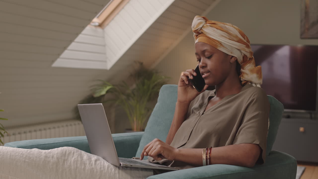 Afroamerikansk kvinde foretager telefonopkald under arbejde på bærbar computer