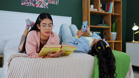 two women relaxing in bedroom reading books and using mobile phone