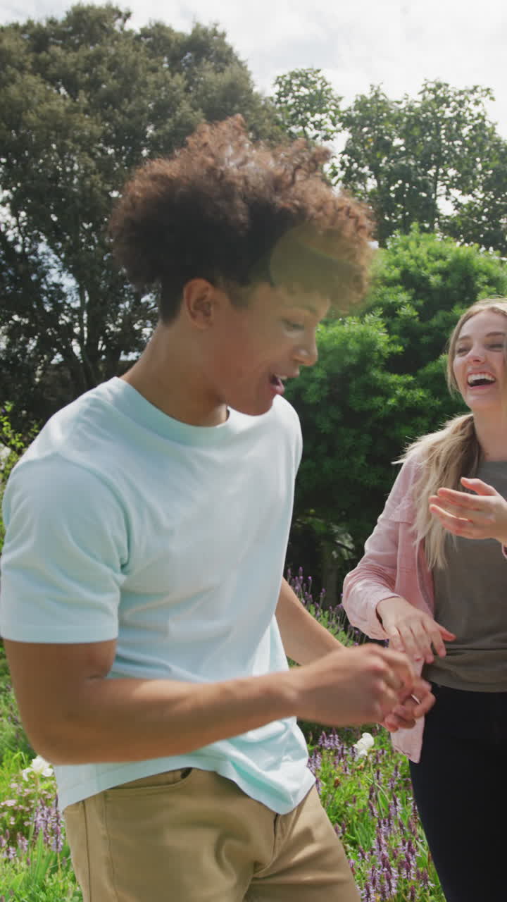 video vertical de una pareja feliz y diversa jugando en el jardín en un día soleado