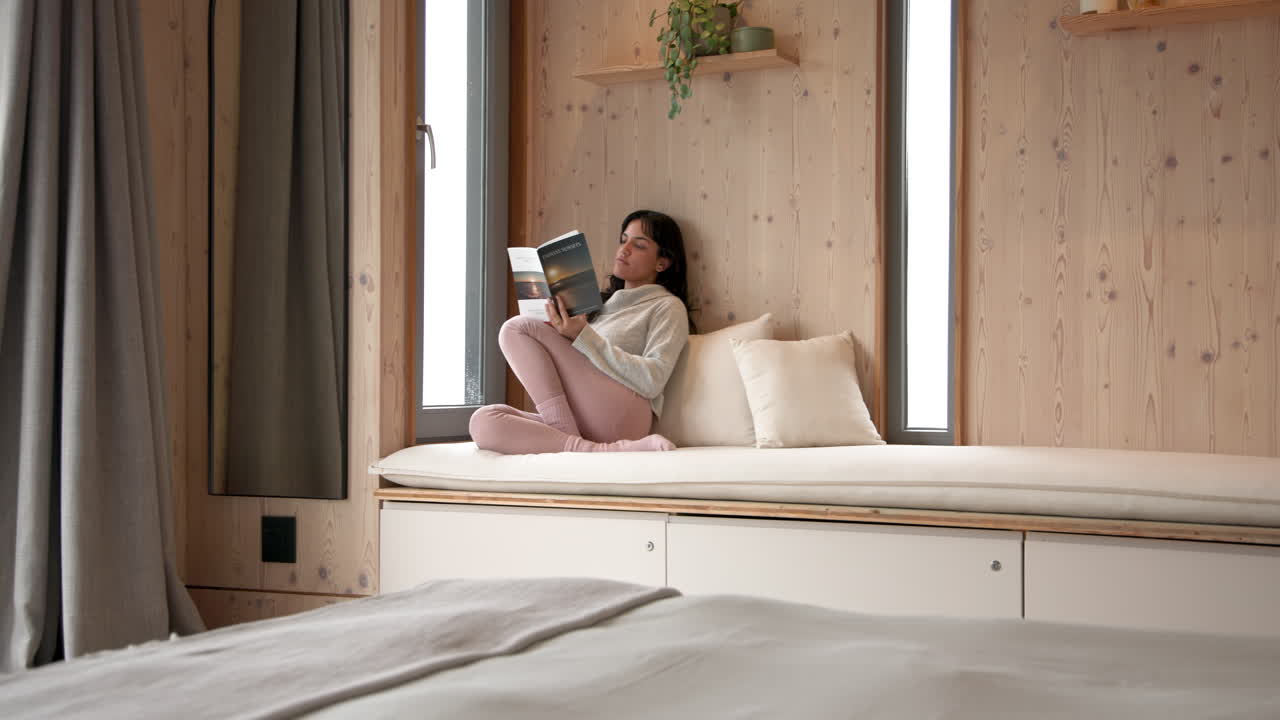 Relaxing at home, woman reading book on cozy window seat, copy space