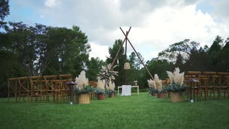 outdoor wedding venue arranged with many wooden chairs, pampas grass decoration, bohemian style