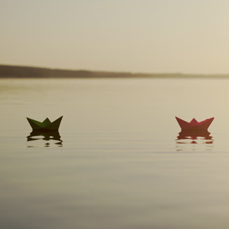 paper boats on water at sunset. nice homemade ships floating near the stones on the evening lake. freedom and hope concept.