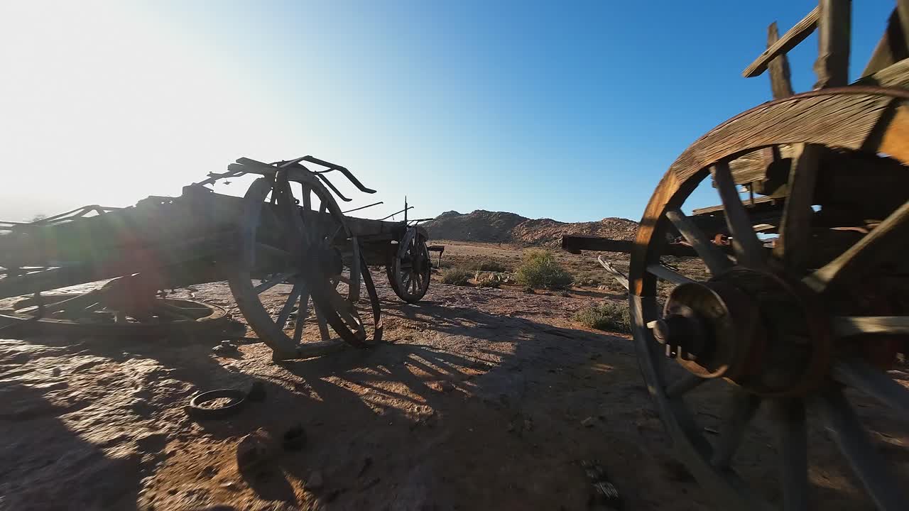 Low FPV proximity aerial flies past antique wagons in desert landscape