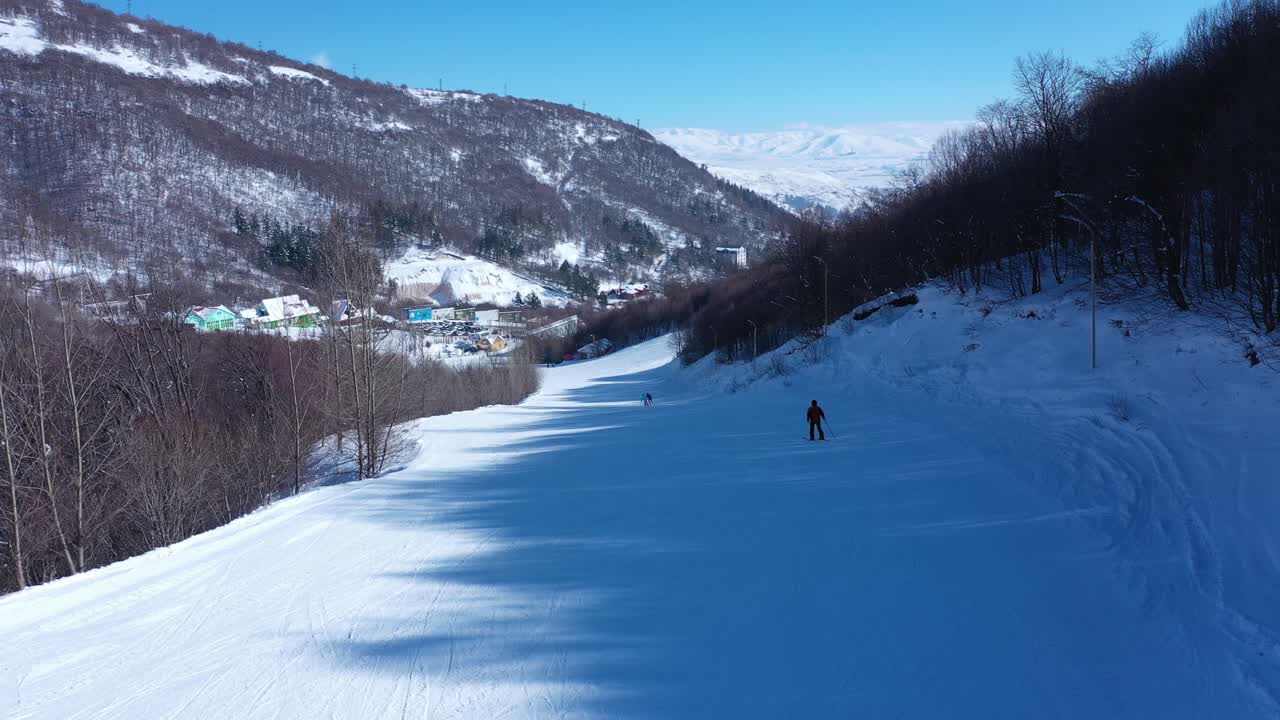 Ski slope winds across snowy mountain terrain with groomed trails and distant skiers moving through winter landscape
