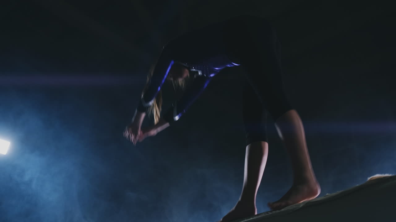 Women's Artistic Gymnastics. In slow motion in the smoke, the girl performs complex elements of the Olympic program on a balance beam.