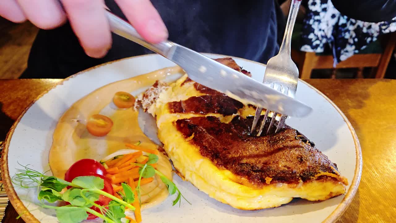 Close up of fluffy omelet sliced with fork, knife in relaxed cafe dining setting