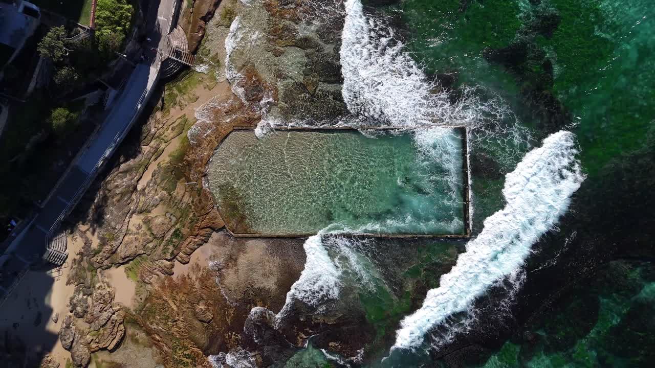 Turquoise rock pool beside rocks and foamy ocean in Cronulla captured from above, Sydney NSW Australia