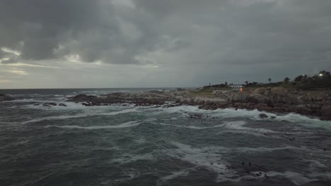 Drone-flying-sideways-just-over-the-sea-at-Camps-Bay-beach-in-Cape-Town,-South-Africa---It's-a-cloudy-day-and-the-sea-waves-are-crashing-against-the-coastline