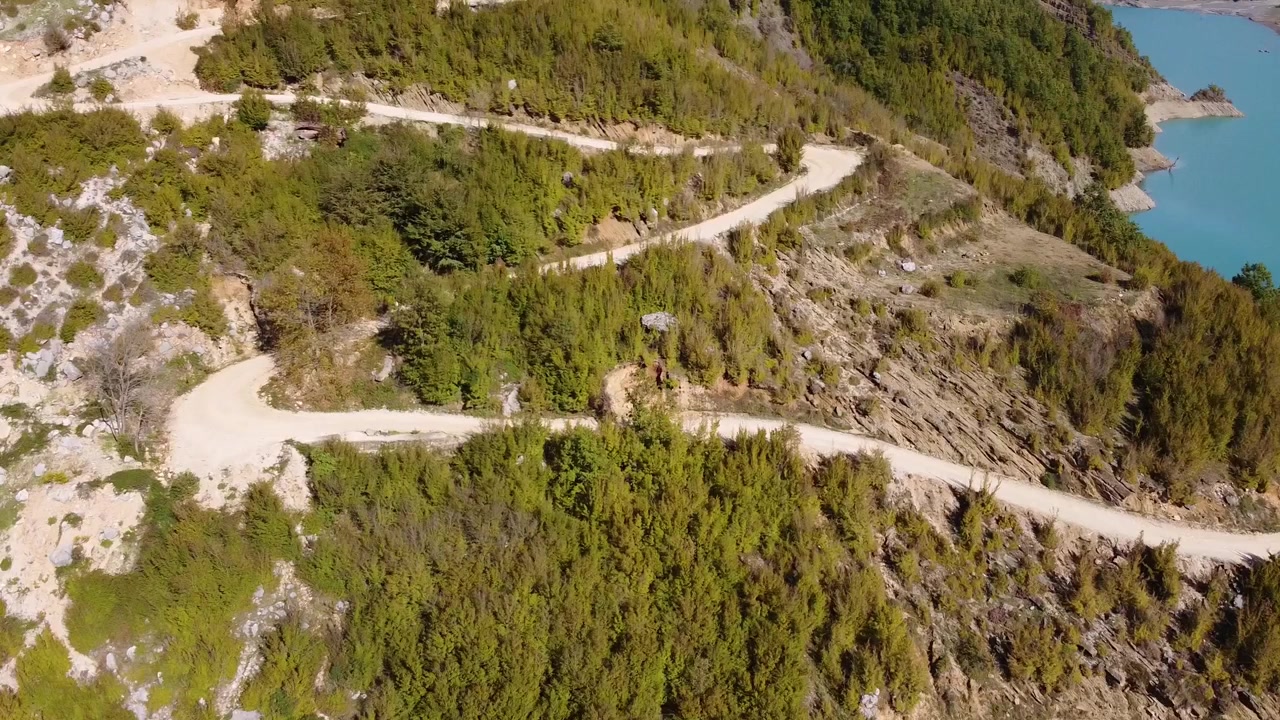 Dronekuva tien yläpuolella Albanian vuoristossa, luonnonkaunis maisema turkoosilla järvellä