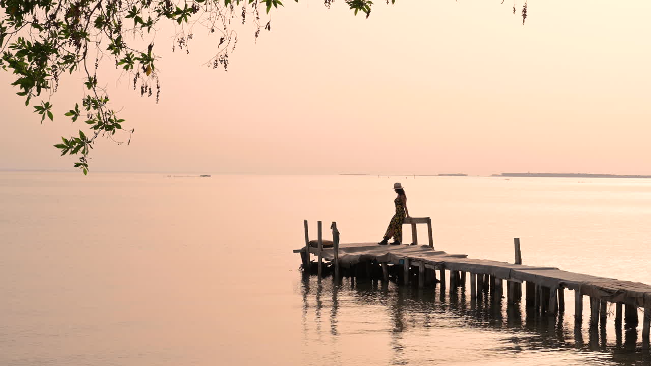 Woman on a wooden pier contemplating the peaceful sunset over the water