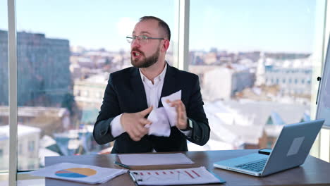 irritated businessman at workplace. nervous man in suit sitting at his working place and throwing papers. businessman talking angrily to someone in office.