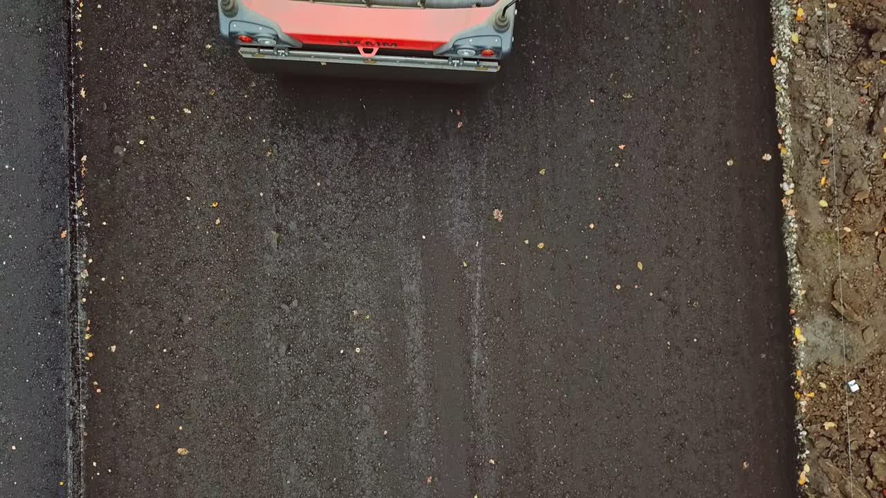 Close-up of roller machine pressing new asphalt. Top view of a spinning wheel of a steamroller while laying black asphalt. Drone view.