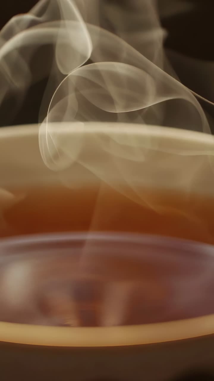 Vertical video: Rising steam from heat in ceramic coffee cup in dim cafe, curling, growing, fading