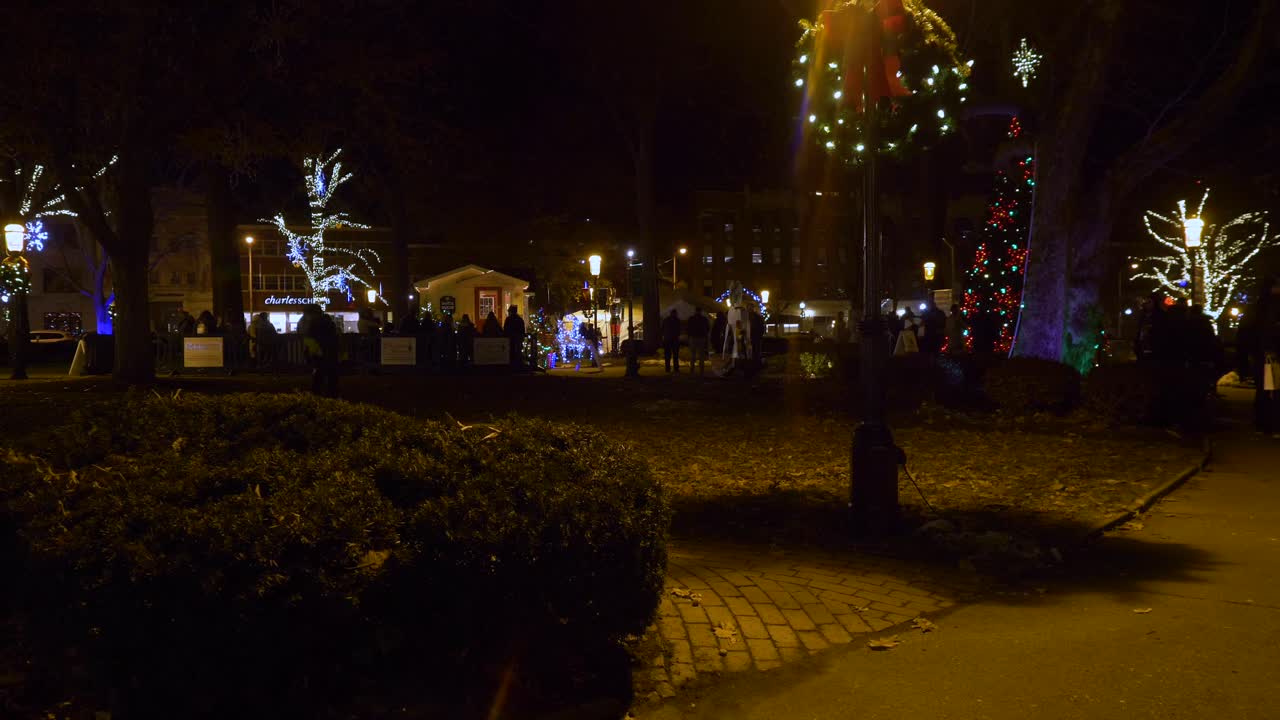 4K: Families walk through a Christmas decorated park at night on their way to see Santa