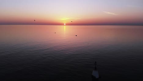 Eine-Herde-Von-Möwen,-Die-Bei-Einem-Sonnenuntergang-über-Die-Navigationsmarkierung-Und-Den-Endlosen-Ruhigen-Tropischen-Ozean-Fliegen