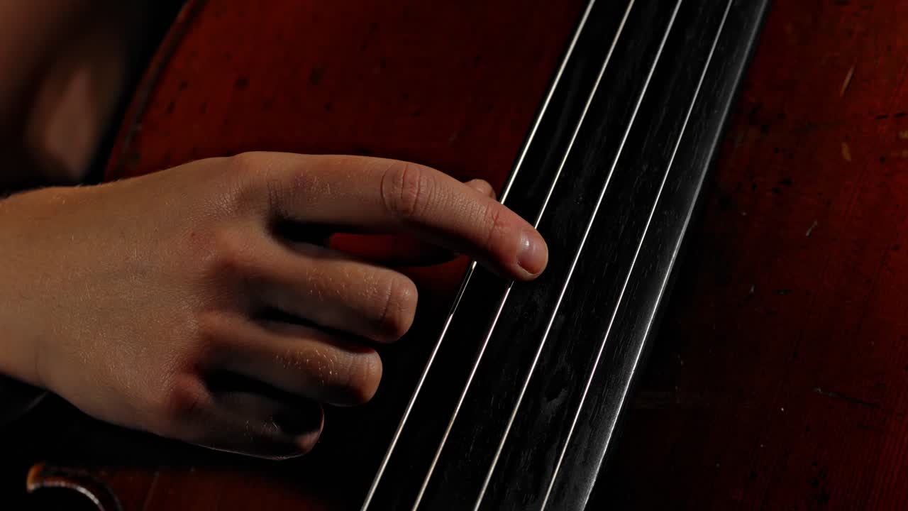 un primer plano extremo de una persona tocando las cuerdas de un contrabajo de violonchelo