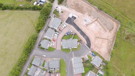 drone exterior view of a new build housing estate in the united kingdom, showing modern homes, paved streets, and green fields in a community setting