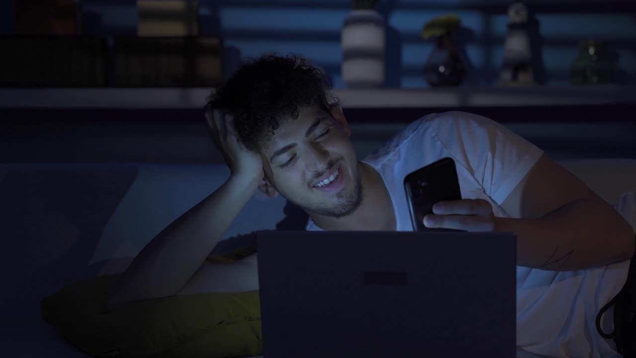 joven feliz enviando mensajes de texto por teléfono por la noche en casa.