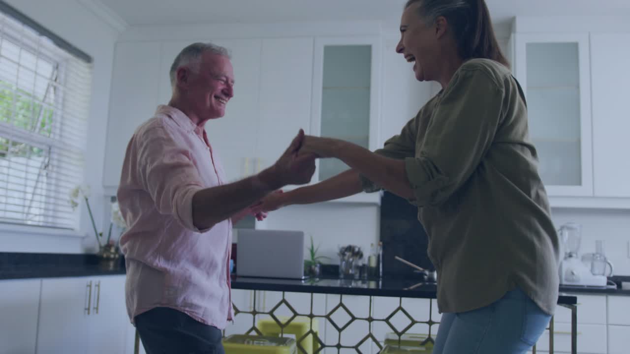 Senior couple clasping and spinning in kitchen, showing rising social engagement via animated icons