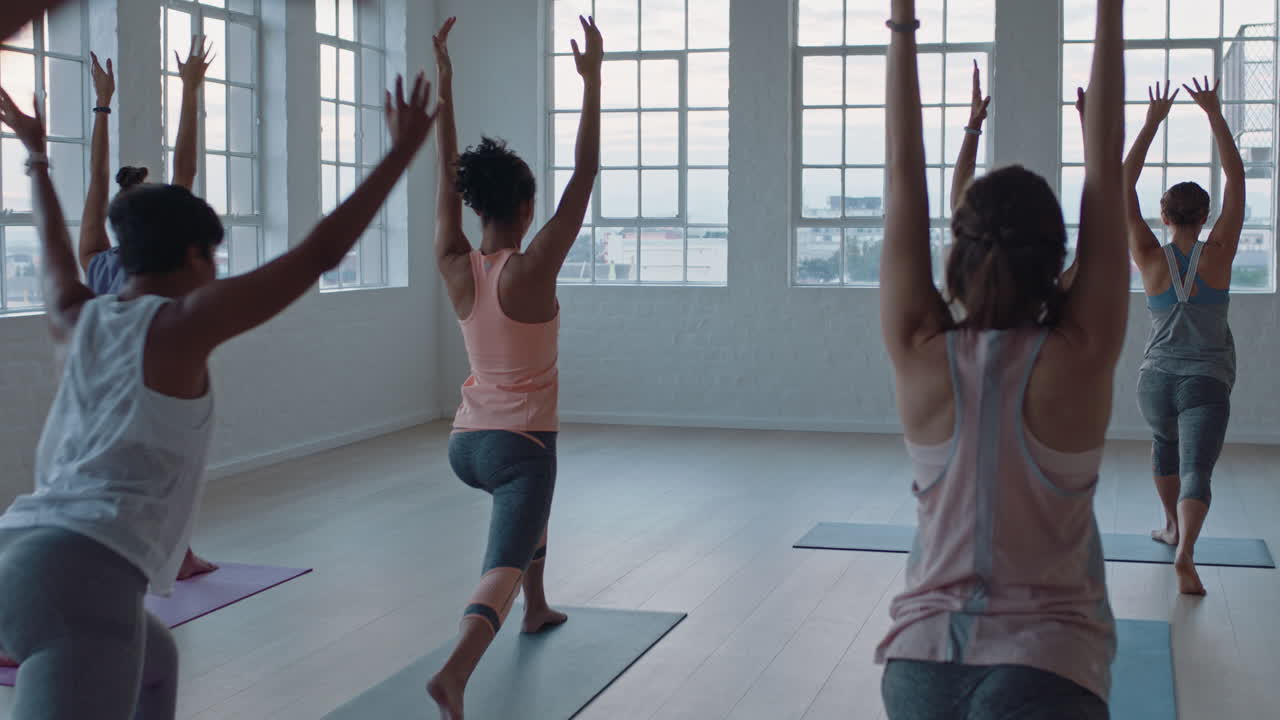 yoga class of healthy women practicing warrior pose enjoying exercising in fitness studio instructor leading group meditation teaching workout posture at sunrise