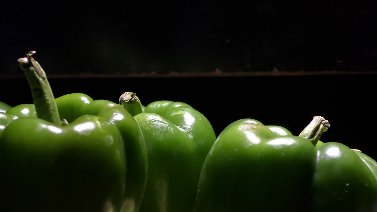 Green capsicums in the dark with light falling on them