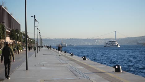 people walking along a waterfront with a bridge in the distance