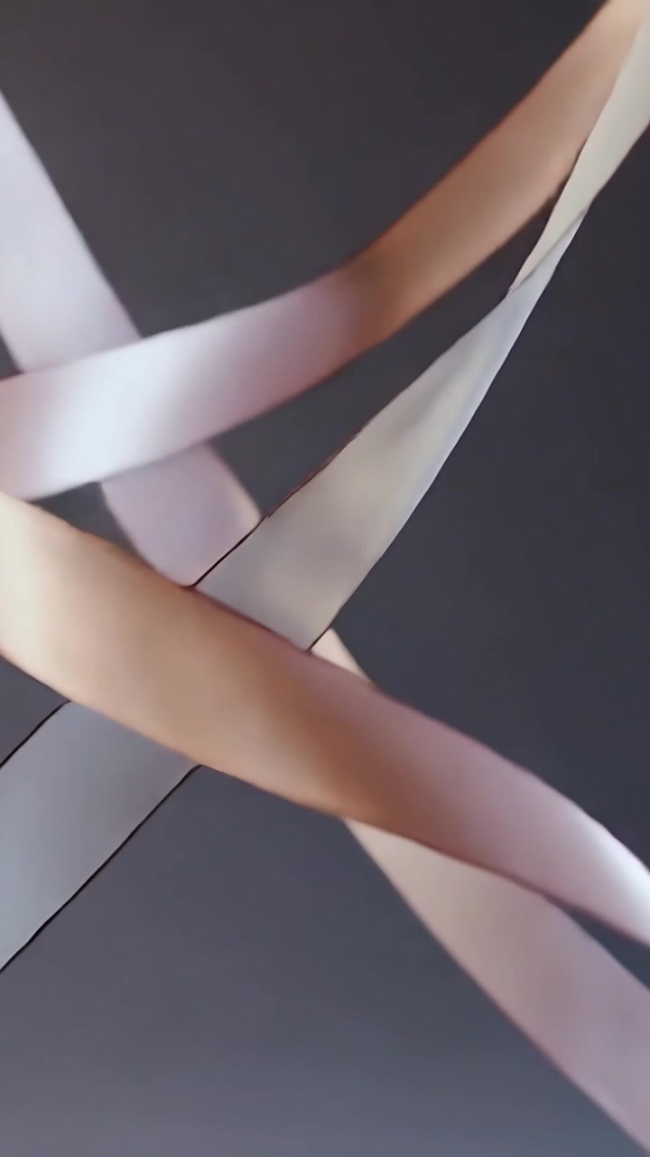 Video verticale: Telecamera che panoramica riprendendo nastri di raso rosa pallido che si attorcono in studio, una mano che tira