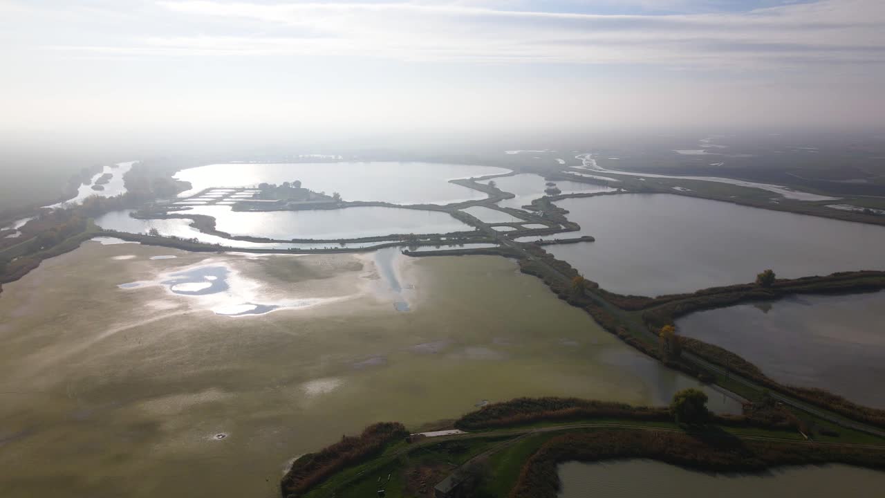 A large fish farm with misty skies and reflective water surfaces at dawn, aerial view