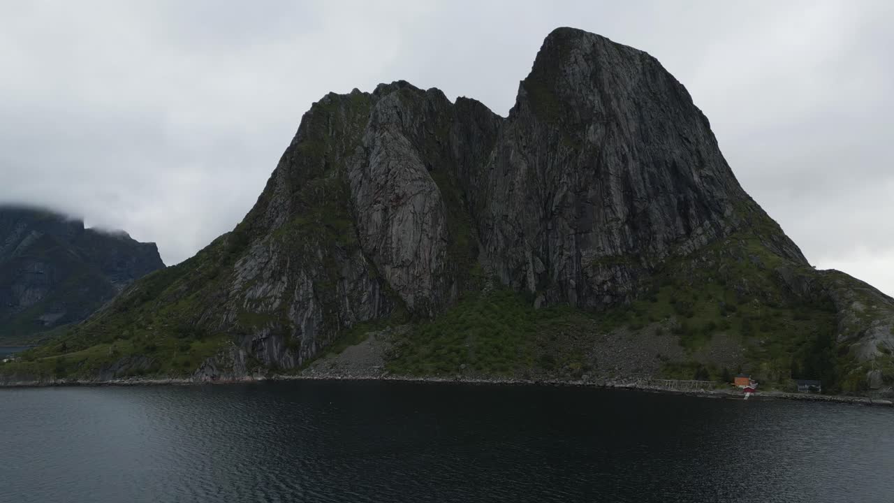 Flying towards the iconic mountain in Hamnoy, Lofoten, Norway with the fisher village surrounded by this mountain with the drone flying above the ocean sea water